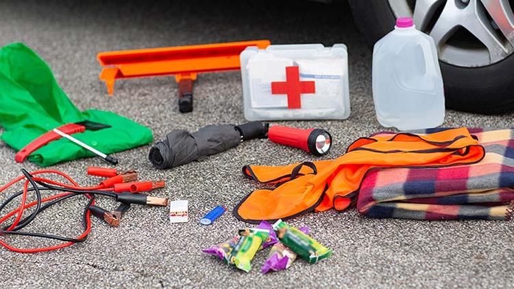 一壶水, 急救箱, 手电筒, umbrella and other emergency kit supplies upacked on the street next to a car tire.